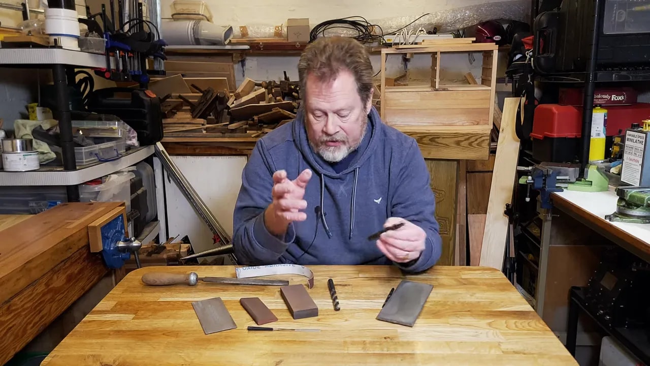 Diamond plate and abrasive stones arranged on a workbench while explaining hand sharpening of a drill bit