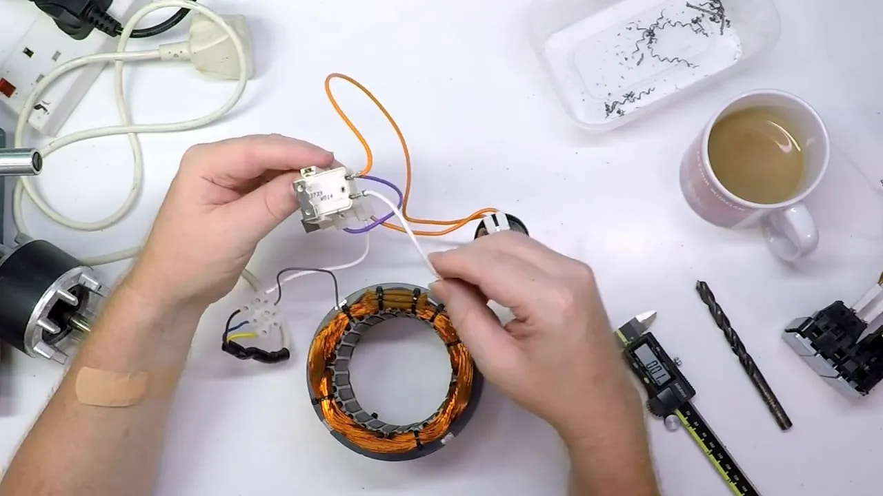 Control switch module held above a single-phase motor stator coil with wiring leads visible