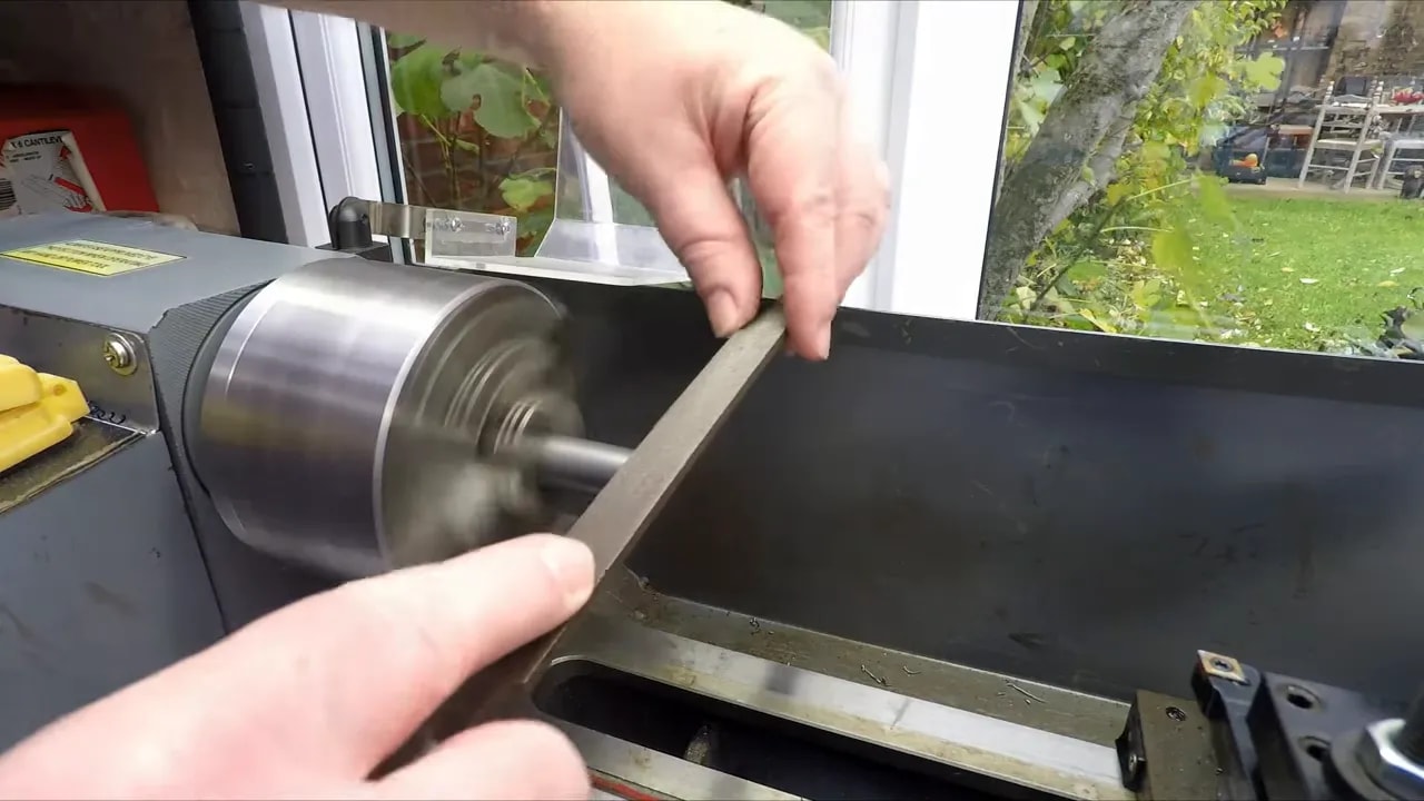 Manually deburring the end of a bar held in a lathe chuck with a file
