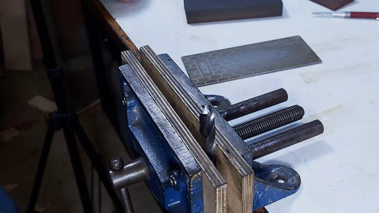 Wide view of drill bit clamped in vice with diamond plate positioned for honing