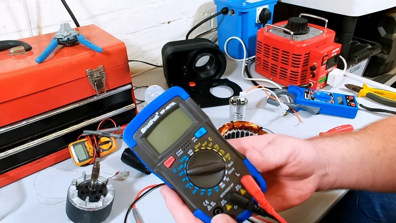 LCR meter held above the bench with stator winding and tools visible