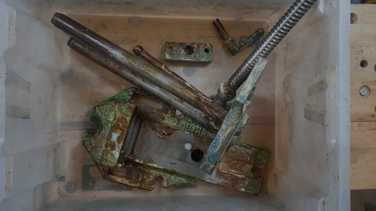 Paint-stripped vice parts lying in a plastic tub after soaking