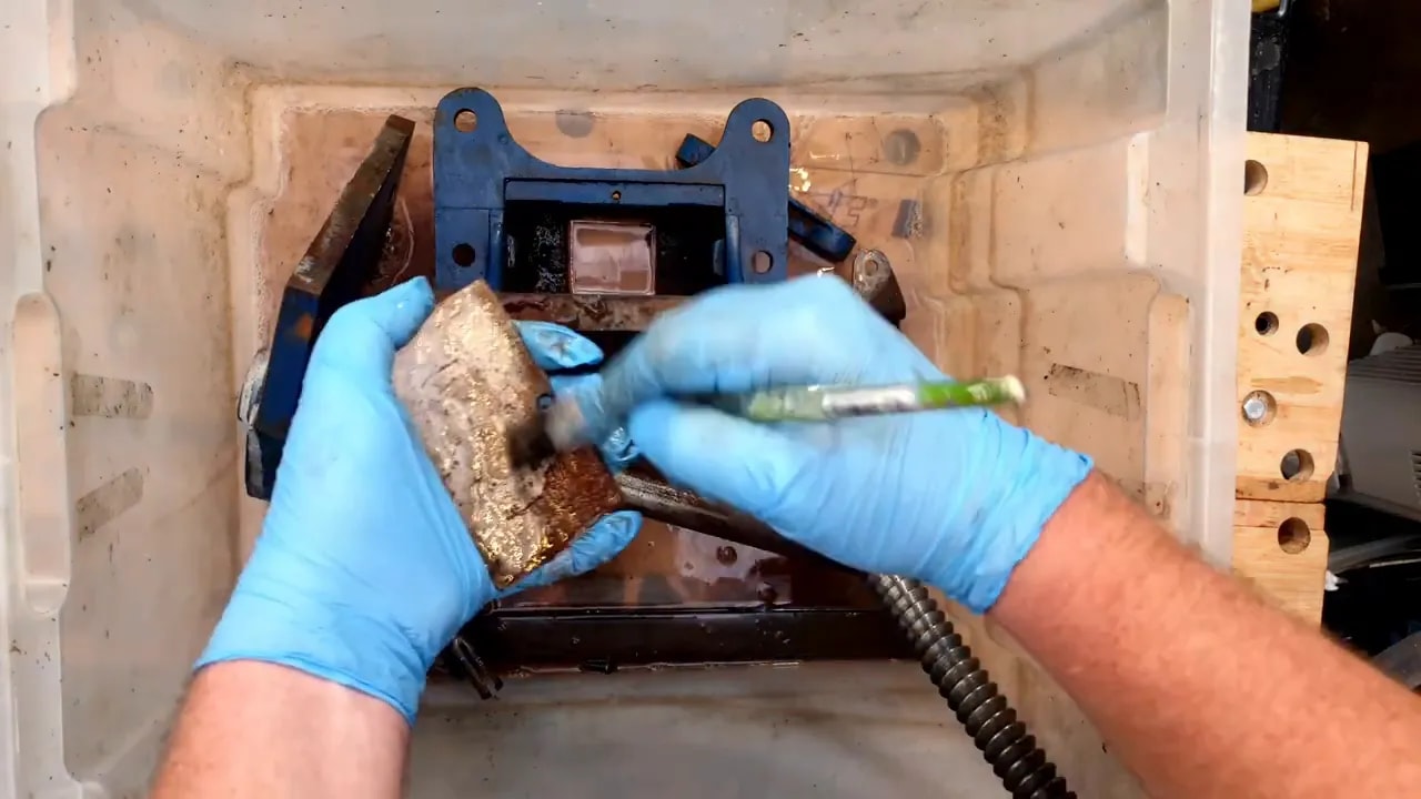 Blue gloved hands scrubbing greasy vice components in a plastic tub