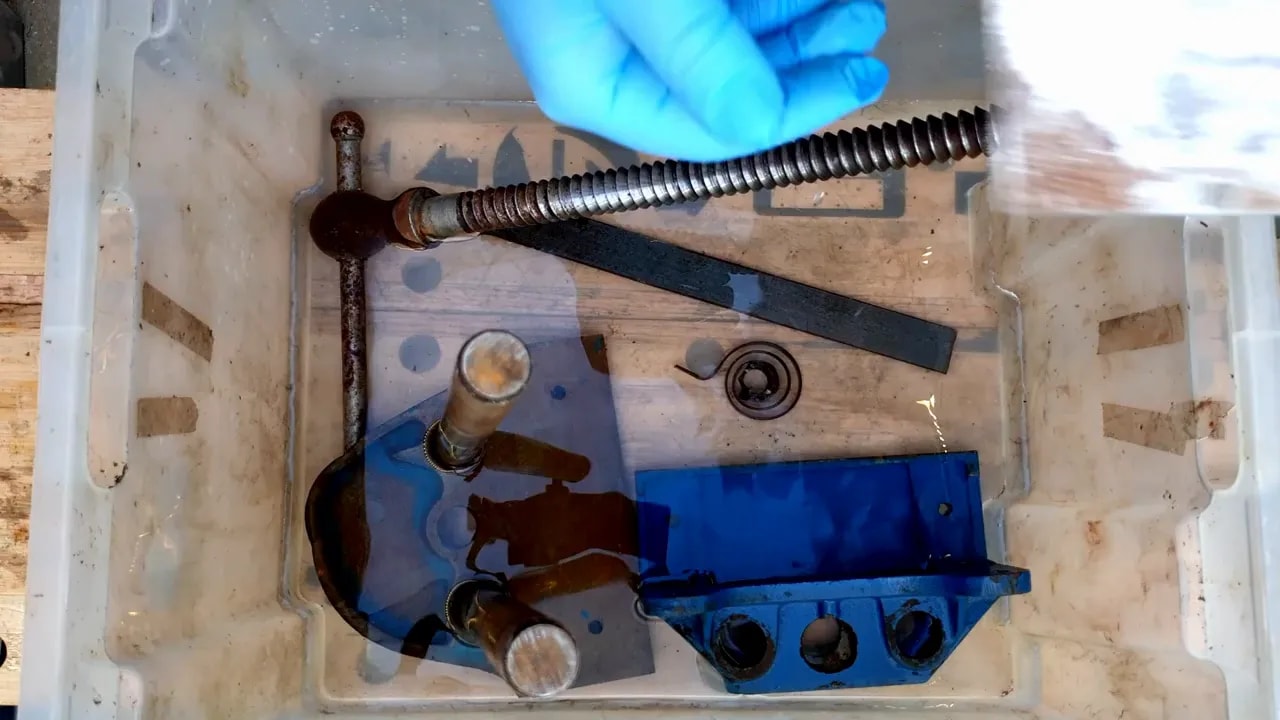 Rusty vice parts, screws and steel components immersed in a clear plastic tub of solution
